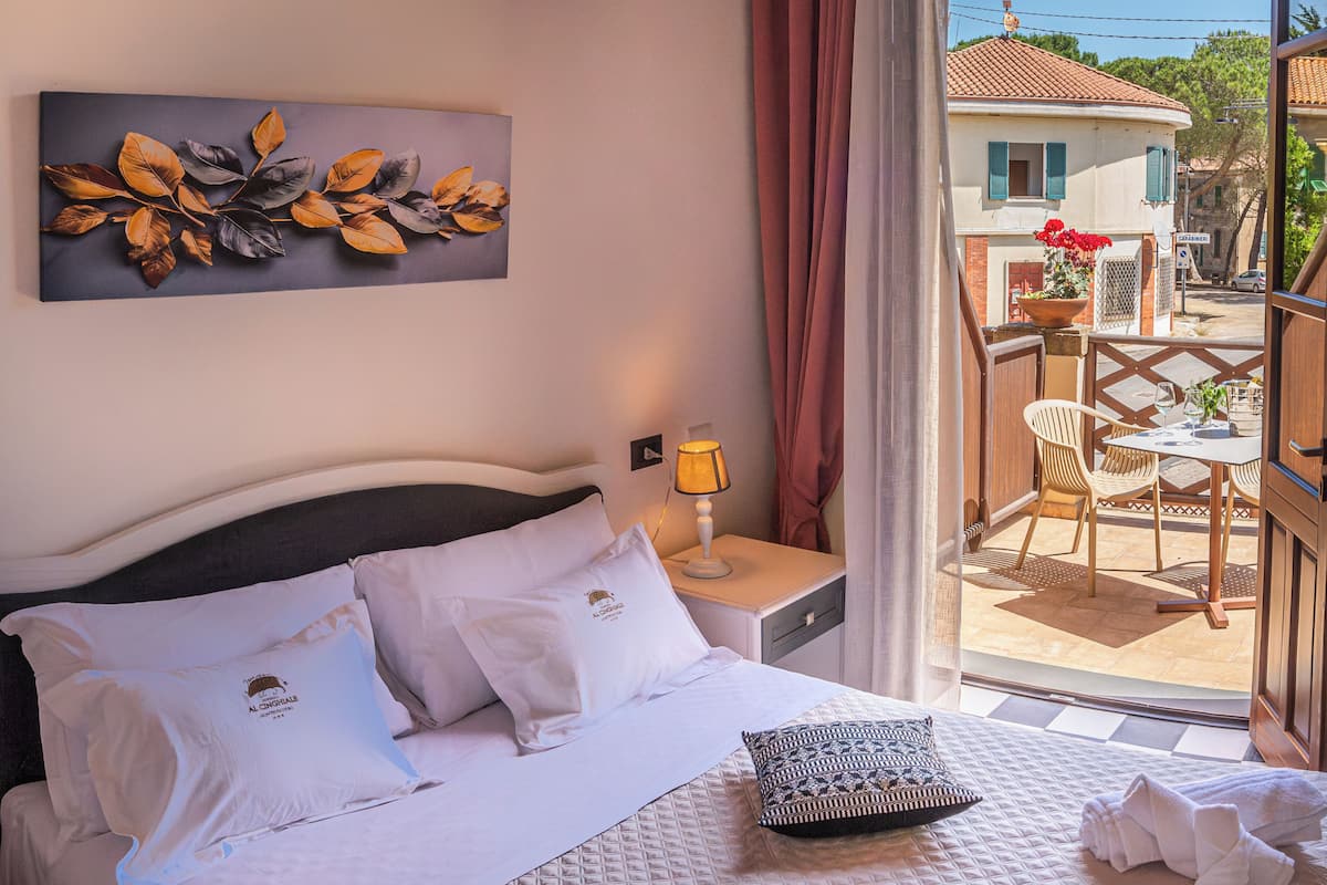 A hotel room with a bed, a nightstand, a lamp, a view of the outside, and a wall decoration.