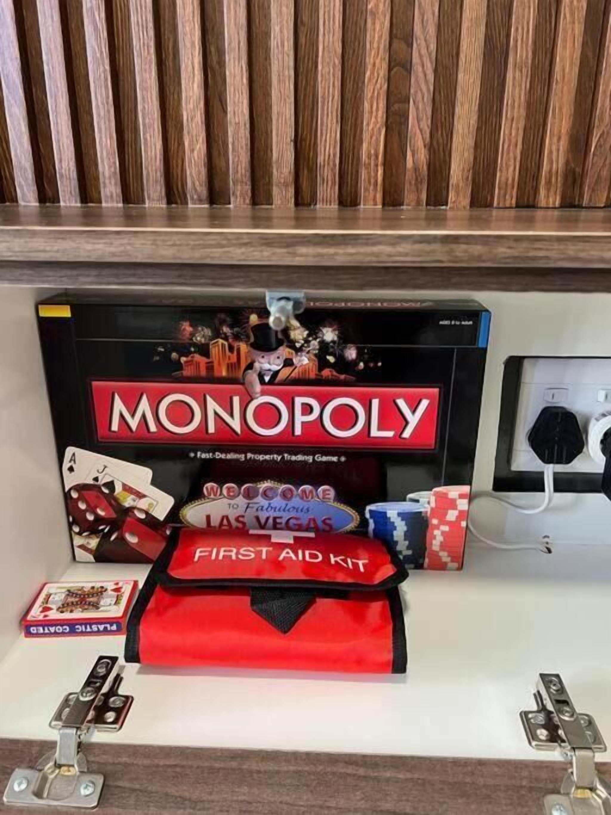 A Monopoly game box with a first aid kit and playing cards on a wooden shelf.
