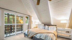 A bedroom with a large bed, a nightstand, and a window with a view of trees. - Zephyr Chalet Home for 8 (Zephyr Cove)