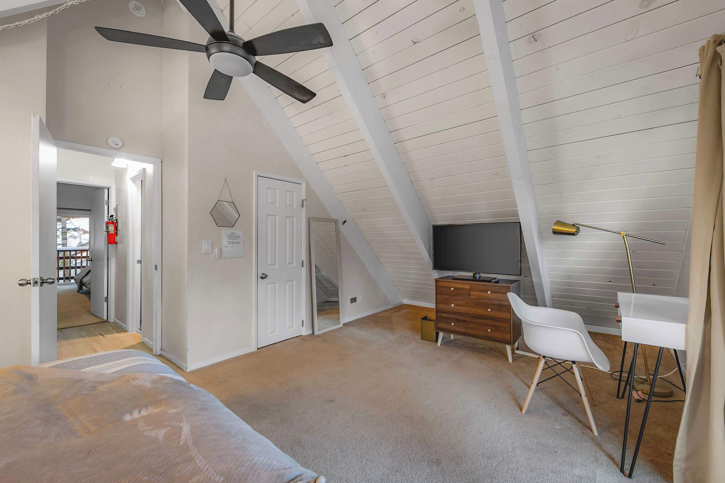 Une chambre avec un plafond en pente, un ventilateur de plafond, un lit, une commode, un téléviseur et un bureau avec une chaise.