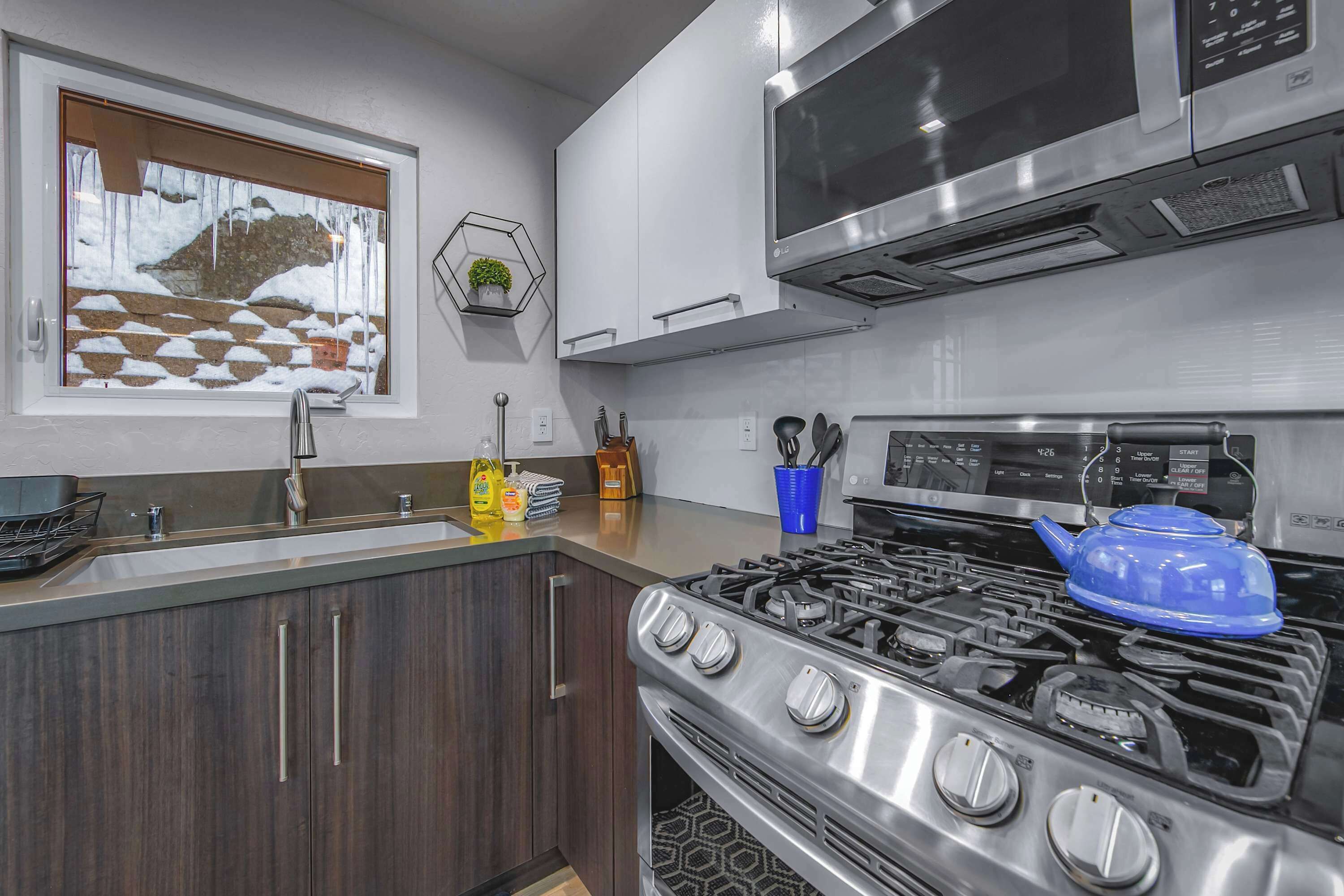 A modern kitchen with a stainless steel stove, a microwave, and a window with a view of a snowy landscape.