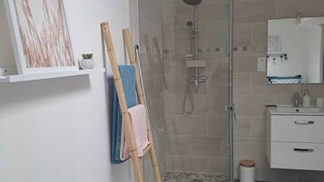 Casa de banho com cabine de duche em vidro, lavatório branco com espelho e toalheiro com duas toalhas.