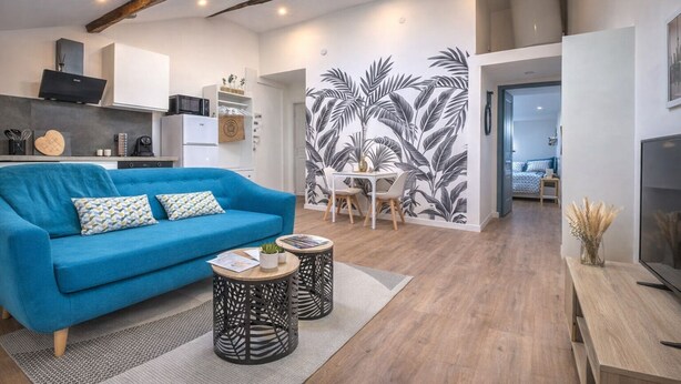 Ein modernes Wohnzimmer mit einem blauen Sofa, einem Essbereich mit weißem Tisch und Stühlen sowie einer Küche im Hintergrund.