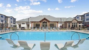 Une piscine avec des chaises longues devant, entourée d’immeubles à plusieurs étages dotés d’une entrée centrale.