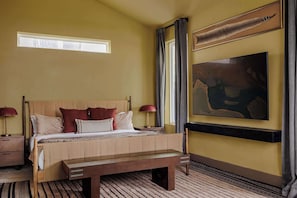 Ein Schlafzimmer mit einem hölzernen Bett, einer Bank, einem Nachttisch, einer Lampe und einem Bild an der Wand.