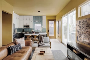 Eine moderne Küche mit weißen Schränken, ein Essbereich mit Tisch und Stühlen sowie ein Wohnzimmer mit einer Couch und einem Couchtisch.