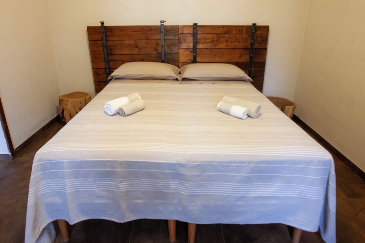 A double bed with a striped bedspread, wooden headboard, and two bedside tables with rolled towels.
