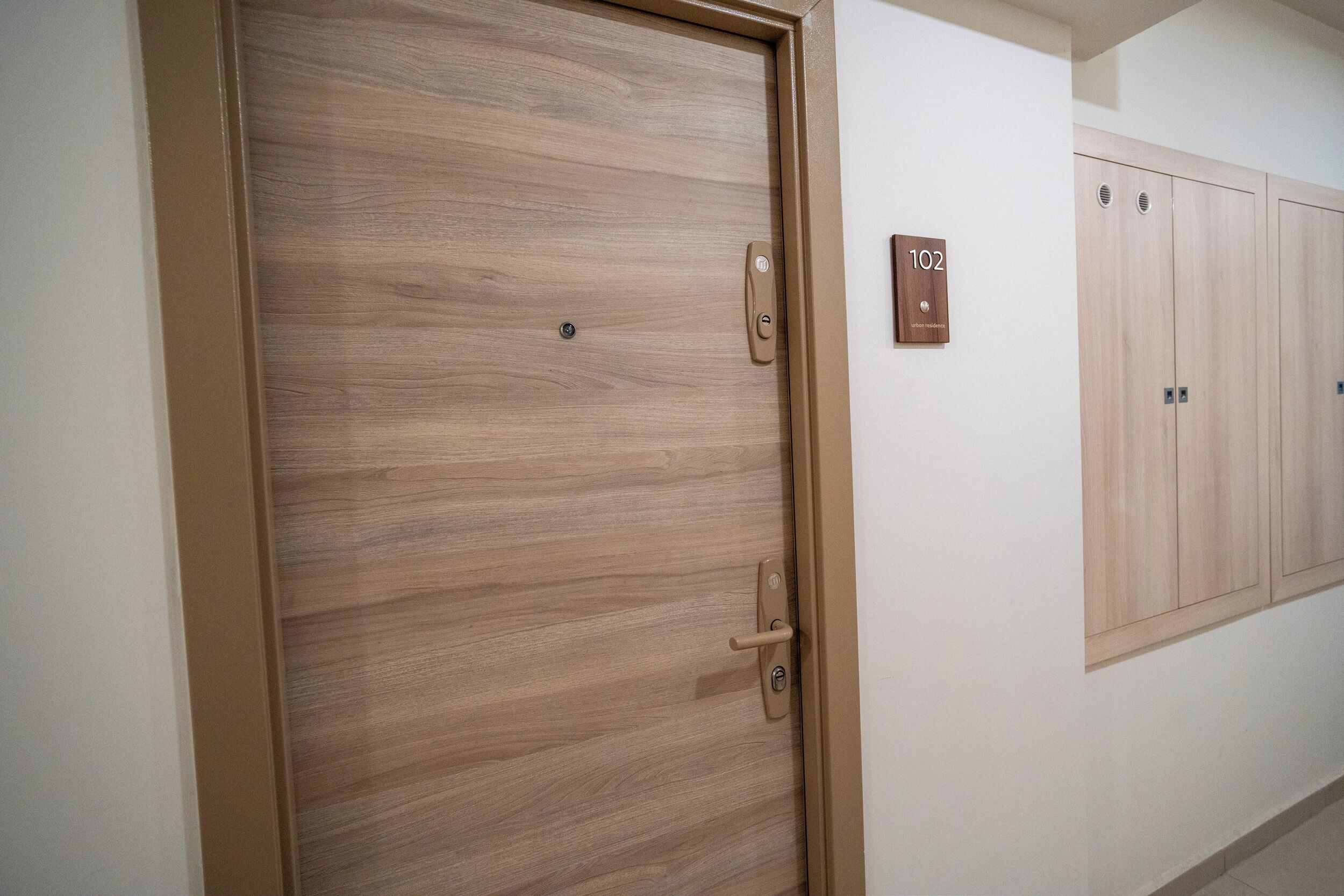 A wooden door with a handle and a lock, a wall-mounted sign with the number 102, and a row of wooden lockers.