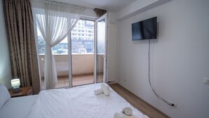 Ein Hotelzimmer mit Bett, Wandfernseher, Vorhängen am Fenster und Blick ins Freie.