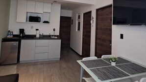 Eine moderne Küche mit weißen Schränken, einer eingebauten Mikrowelle und einer Kaffeemaschine. Es gibt einen Essbereich mit Tisch und Stühlen sowie einen kleinen Blumentopf.