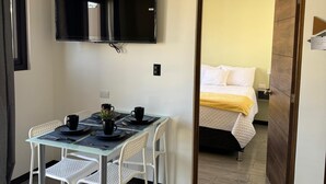 Ein gemütlicher Raum mit Essbereich, Bett und an der Wand befestigtem Fernseher.