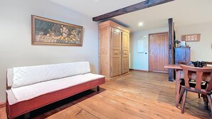 A room with a wooden floor, a sofa, a dining table with chairs, wooden cabinets, and a framed picture on the wall. - La Perle du Ried n°6 - Alsatian charm and tranquillity just a stone's throw from Europa-Park (Boofzheim)