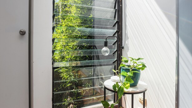 A modern interior with a sliding glass door leading to a balcony, a small round table with a potted plant, and a wooden floor. - Melb suite zen garden A0 F1 (West Melbourne)