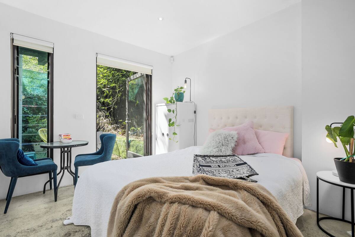 A bedroom with a large bed, a small table, two chairs, and a potted plant.