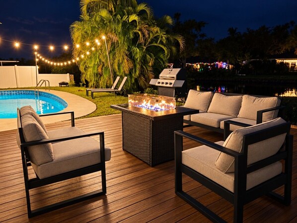 An outdoor deck with a pool, lounge chairs, a fire pit, and a grill area. - Heated Pool • Fire Pit • 10 Min to Madeira Beach & John`s Pass • Sleeps 10 (St. Petersburg)