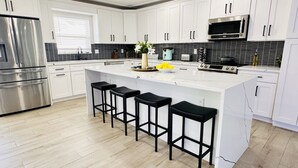 Uma cozinha moderna com armários brancos, uma geladeira de aço inoxidável, micro-ondas e uma ilha grande com banquetas pretas.
