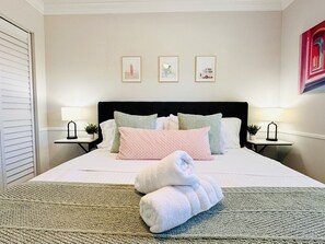 A neatly made bed with a rolled towel, two bedside tables with lamps, and three framed pictures on the wall. - 4-Bed Private Home w/ Pool – 7 Min to Beach & Golf (St. Petersburg)