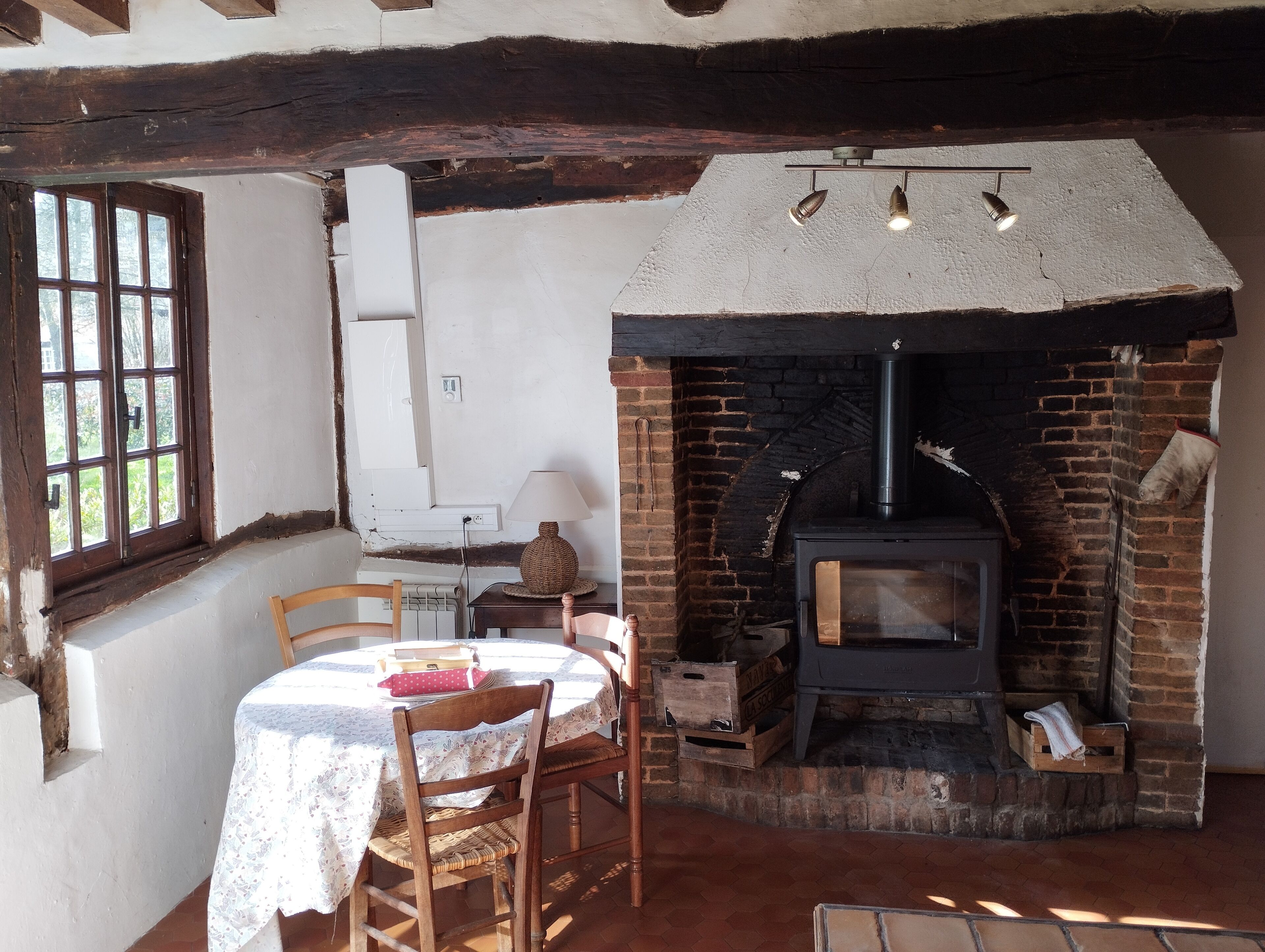 Une pièce rustique avec une cheminée en briques, une table avec des chaises et une fenêtre à carreaux.