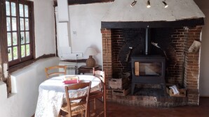 Una habitación rústica con chimenea de ladrillo, una mesa con sillas y un ventanal de varios paneles.