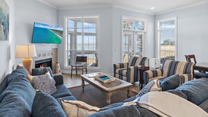 A living room with a fireplace, a television, and a large window with blinds. - ⛱️Bay Views | Tram to Beach | Sandestin Resort | Pool | Vantage Pointe 43☀️ (Miramar Beach)