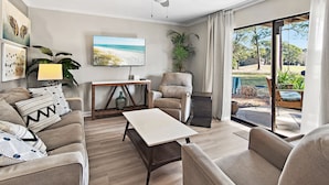 A living room with a sofa, armchair, coffee table, TV, ceiling fan, and a view of the outdoors. - 🏖️Ground Floor 2BR | Pet Friendly | Pools + Golf Course | Seascape 91B🌞 (Miramar Beach)