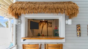 Eine Strandbar mit Reetdach, Holzstühlen und einem Fernseher.