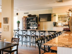 Eine Bar mit einer Theke, Hockstühlen und einem an der Wand befestigten Fernseher.