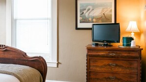 A bedroom with a bed, a dresser, a framed picture of a swan, a television, and a lamp.