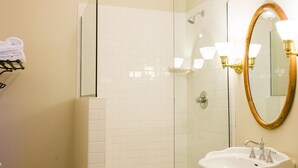 A bathroom with a glass-enclosed shower, a white sink with a gold-framed mirror, and a towel rack with folded towels.