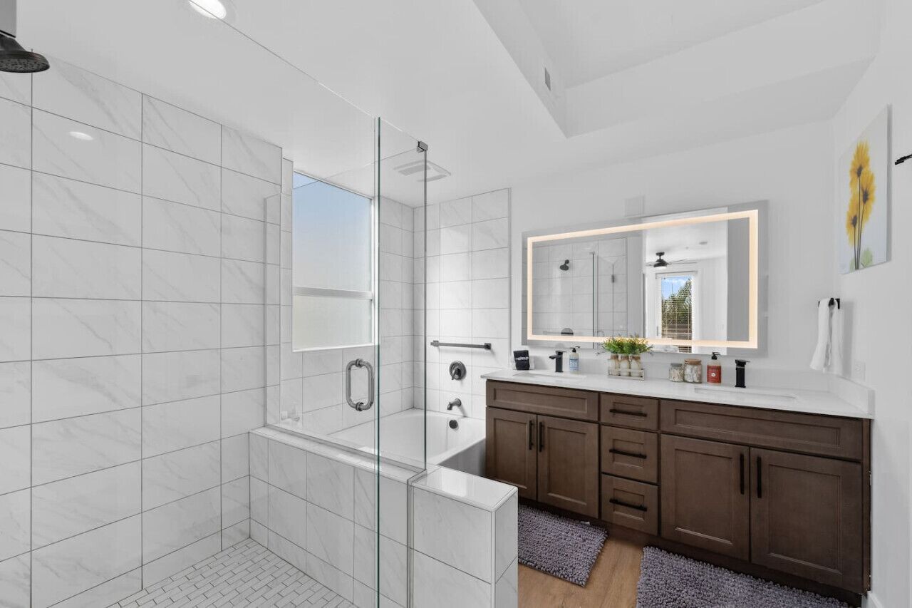 A modern bathroom with a glass-enclosed shower, a large mirror, and a vanity with a sink and cabinet.