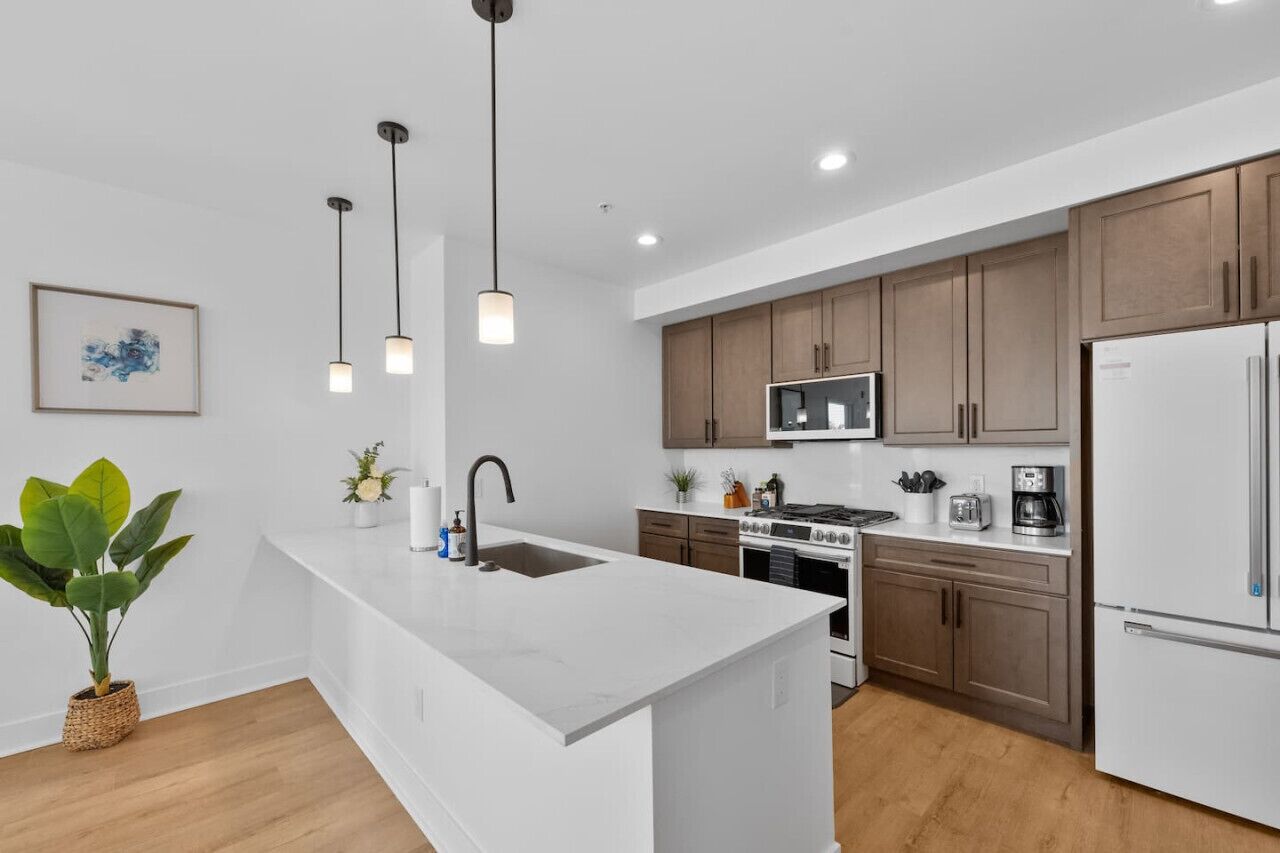 A modern kitchen with white cabinetry, a central island, stainless steel appliances, and pendant lighting.