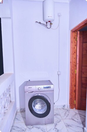Un lavadero pequeño con una lavadora Samsung, un calentador de agua y una puerta de madera.