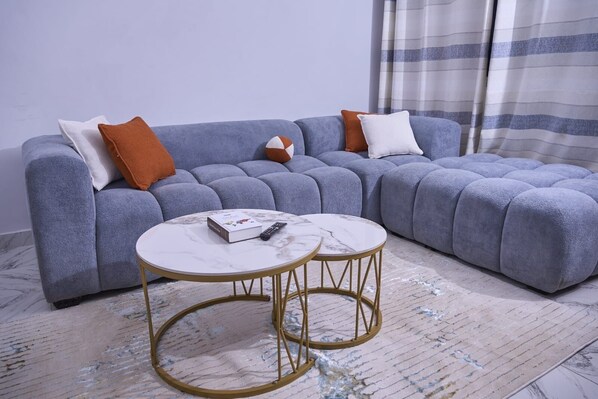 Un sofá modular con muchos cojines, dos mesas redondas con marcos dorados y una alfombra estampada.
