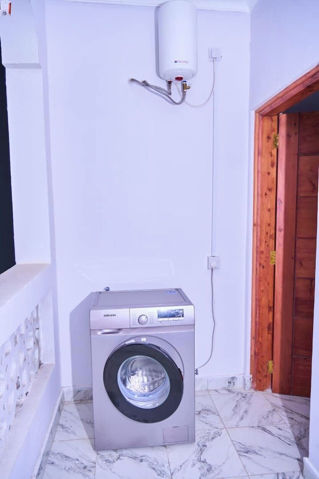 A compact laundry room with a front-loading washing machine, a wall-mounted heater, and a wooden door.