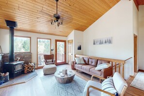 A spacious living room with a high ceiling, a fireplace, a sofa, a coffee table, and a view of the outdoors. - High Country Haven - One Hour from Breckenridge - Private Hot Tub, Pet Friendly! (Jefferson)