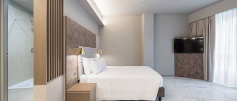 A modern hotel room with a large bed, a bedside table, a TV, and a glass shower area.