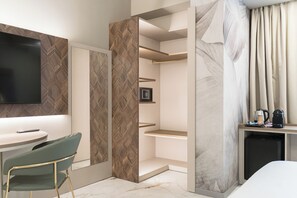 A modern hotel room with a flat-screen TV, a dining area with a green chair, a built-in shelf, a coffee maker, and a small refrigerator. - Baires Guest House (Milan)