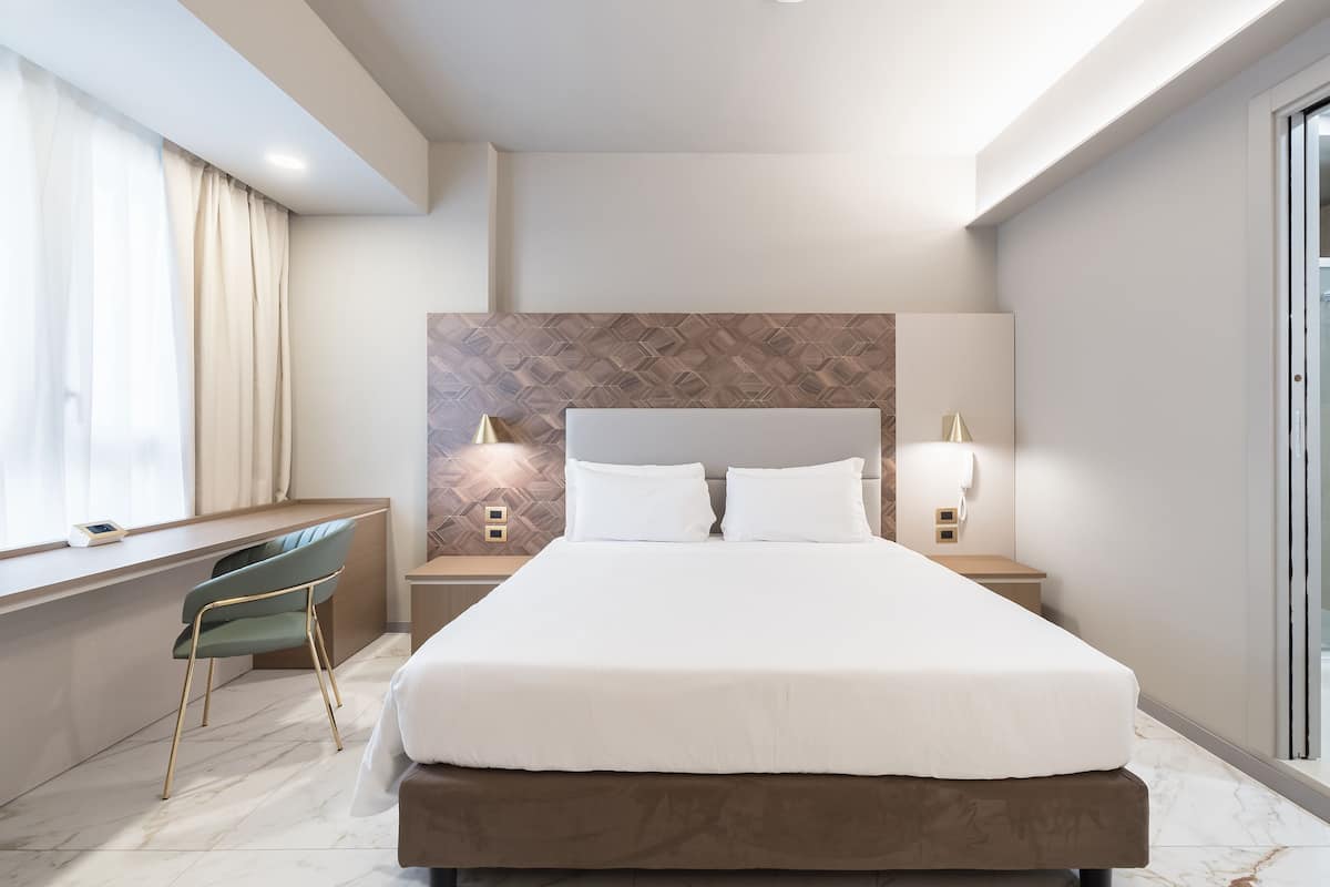 A modern hotel room with a large bed, a desk, and a chair.