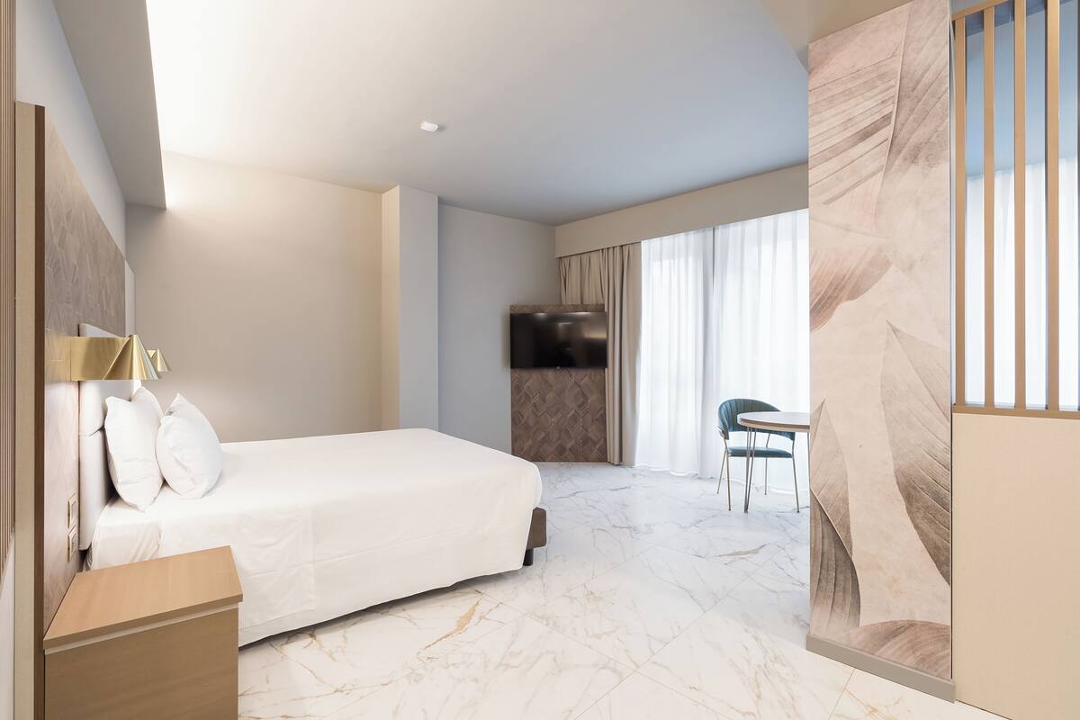 A modern hotel room with a large bed, a desk, a chair, and a television.