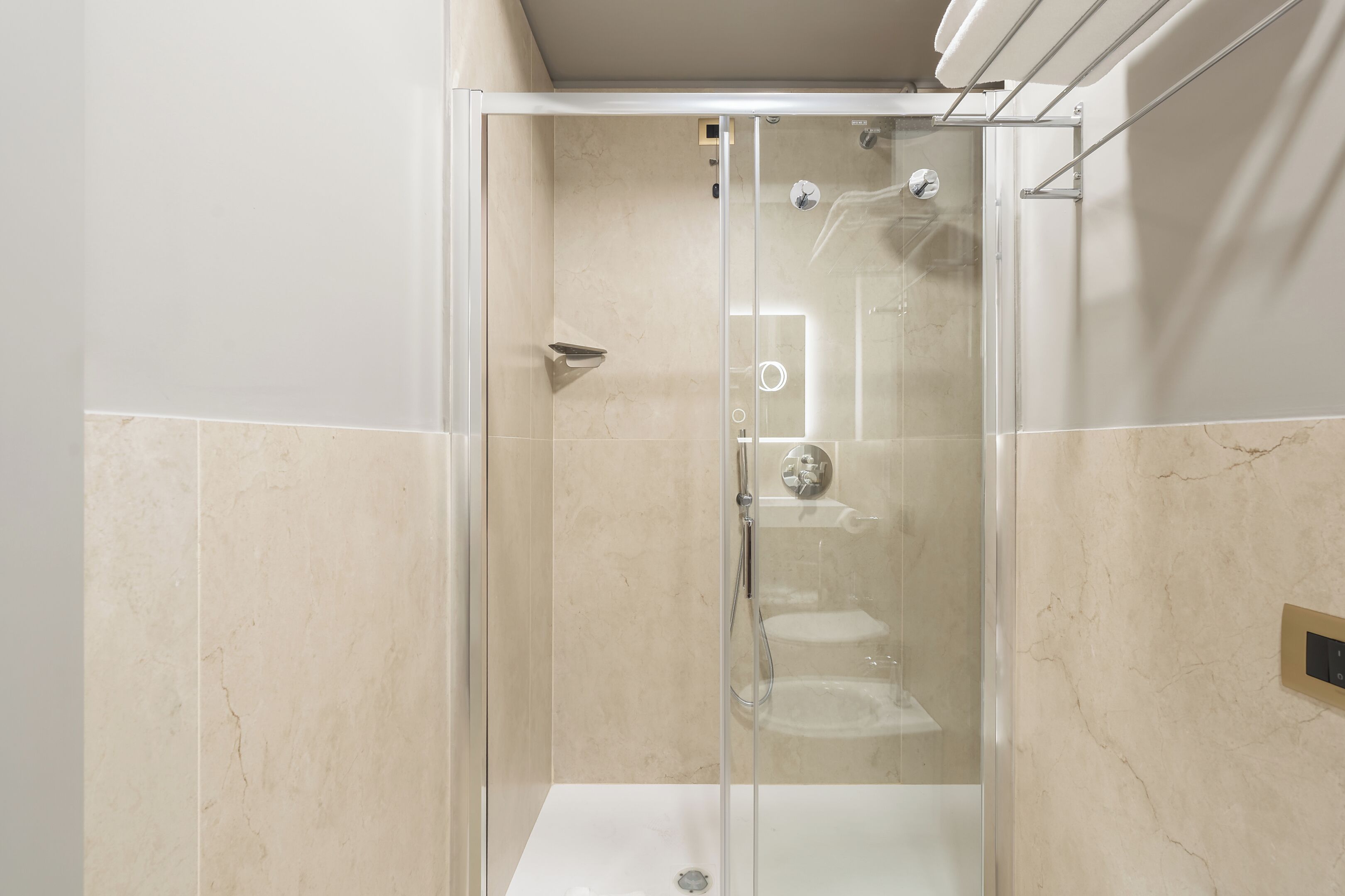 A modern bathroom with a glass-enclosed shower, a white sink, and a marble-tiled wall.