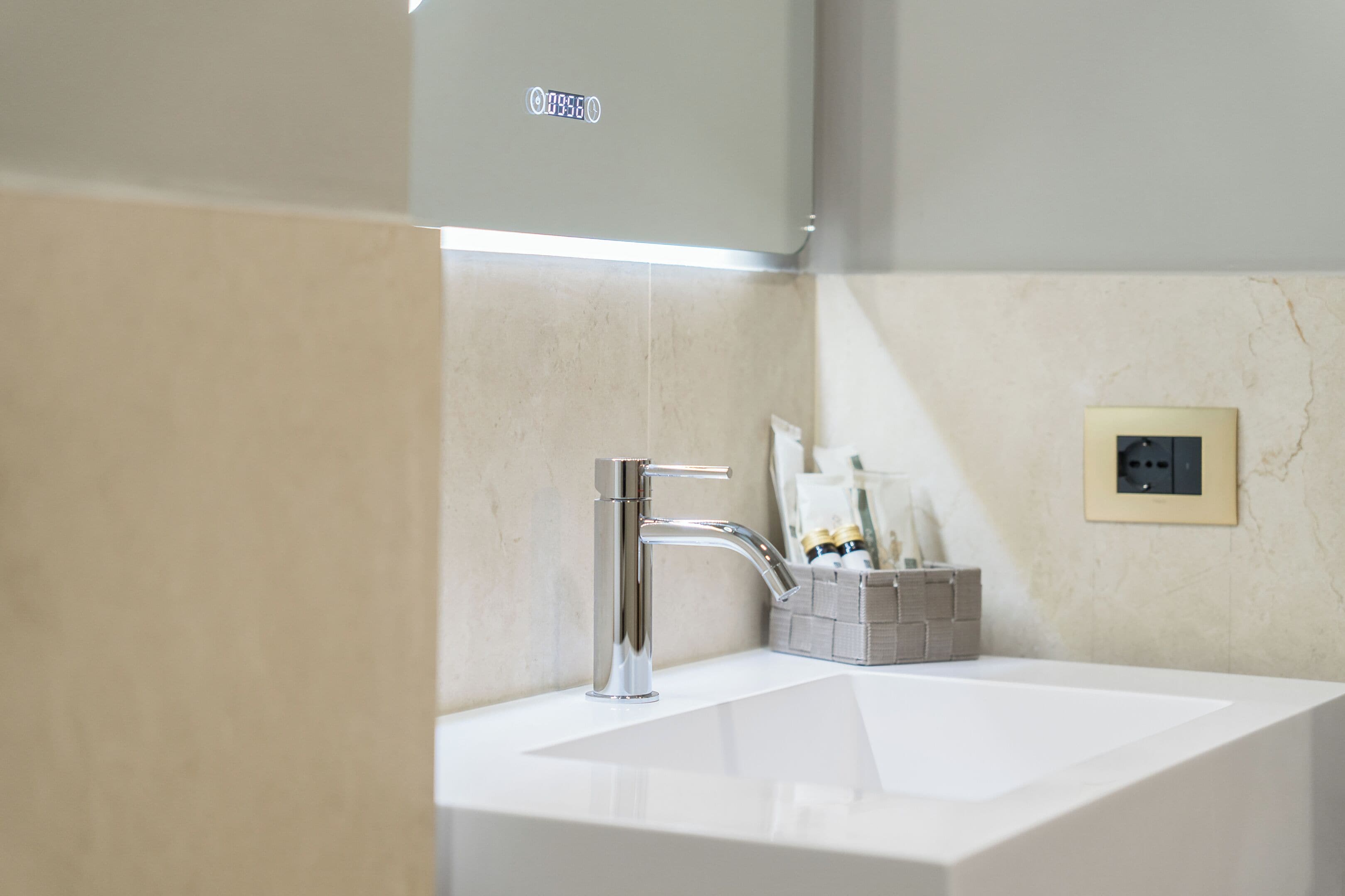 Ein modernes Badezimmer mit einem weißen Waschbecken, einem chromfarbenen Wasserhahn und einer kleinen Ablage mit Toilettenartikeln.