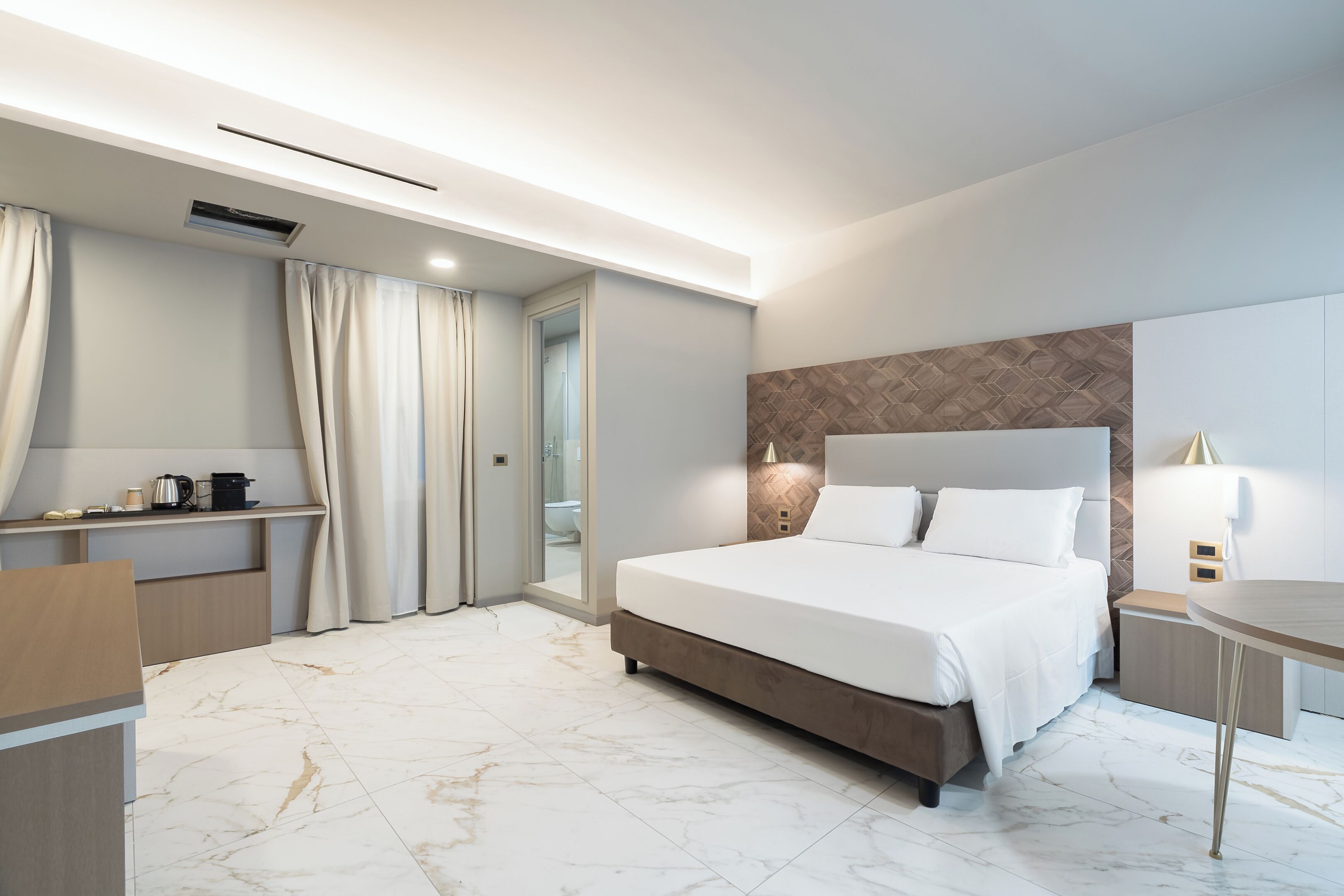 A modern hotel room with a large bed, a desk, and a mirror.