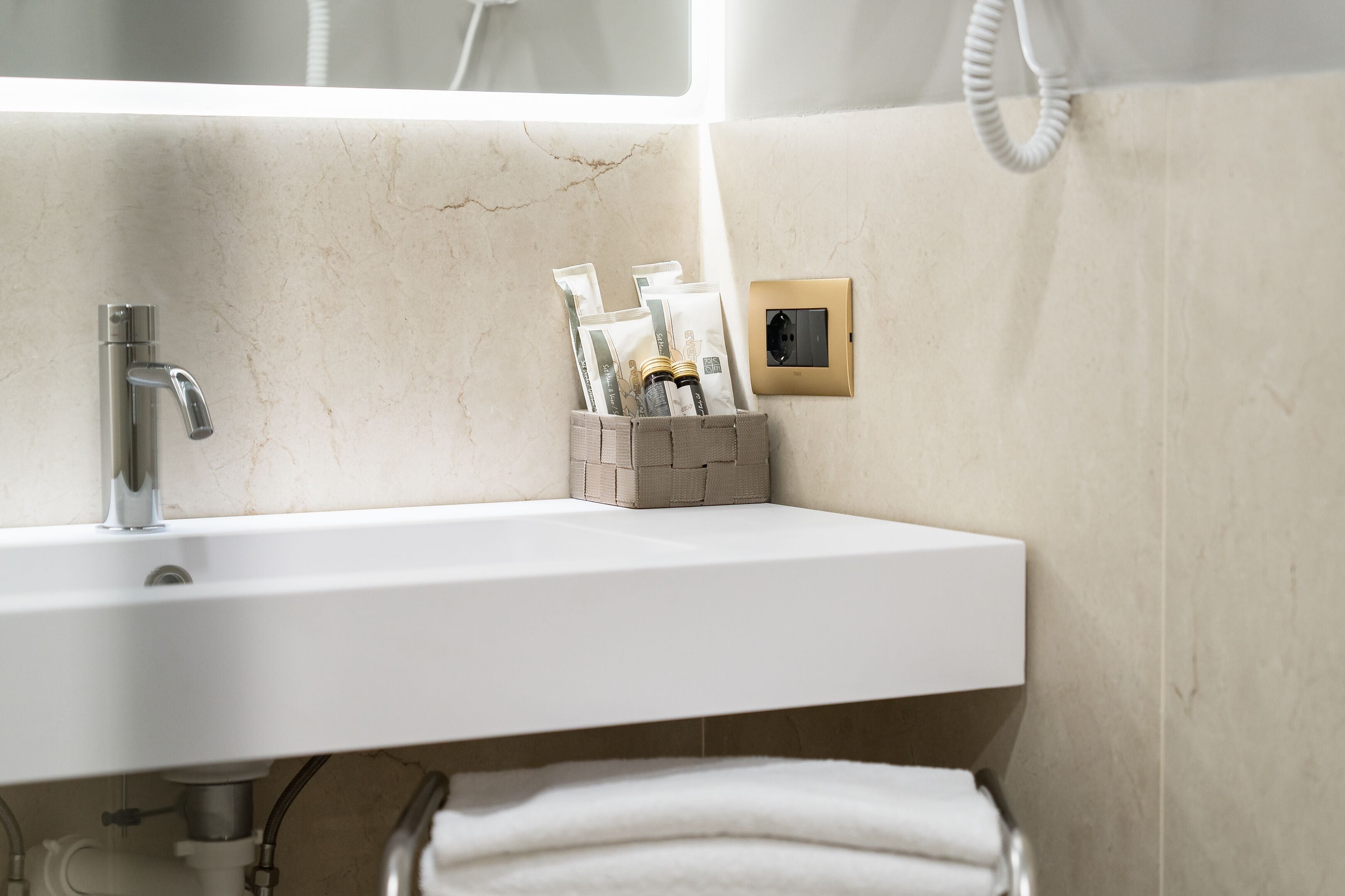A bathroom with a white sink, a towel rack, and a small storage box with toiletries.