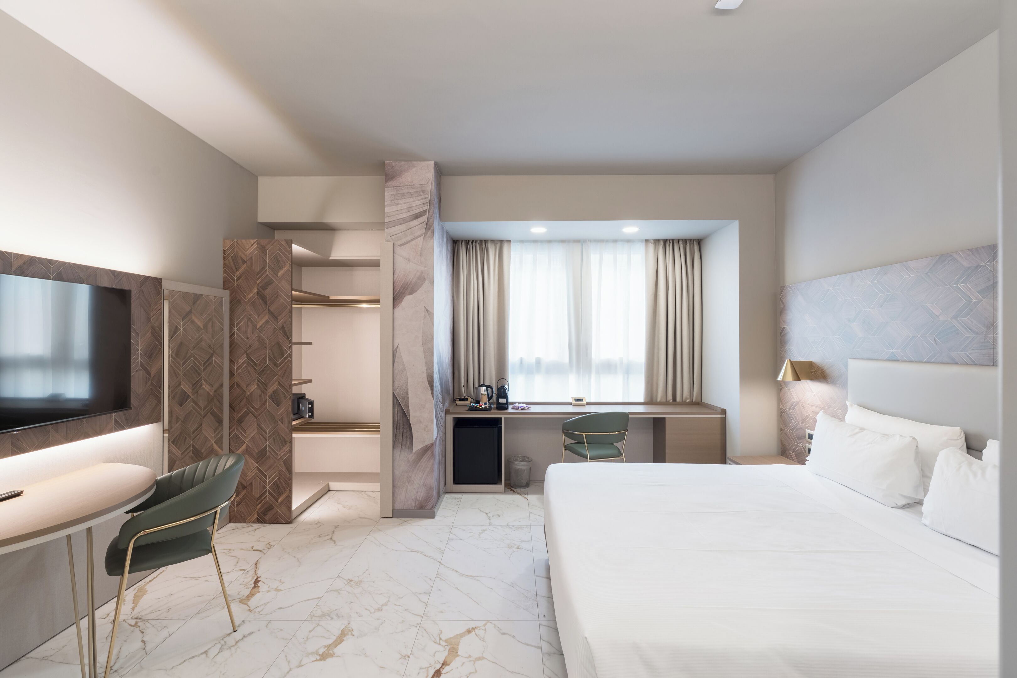 Una habitación de hotel moderna con una cama grande, un escritorio con silla, televisión y minibar.