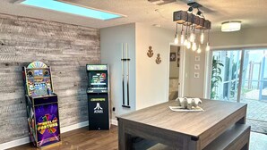 Une pièce dotée d’un plancher en bois, d’une grande table, d’un billard, de bornes d’arcade et d’un luminaire au plafond.
