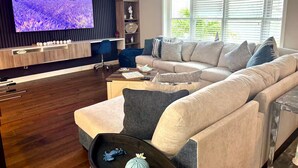 Un salon moderne doté d’un grand téléviseur à écran plat, d’un canapé d’angle, d’une table basse en bois et d’une bibliothèque.