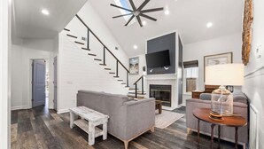 A spacious living area with a staircase, a fireplace, and a television mounted on the wall. - Steps from the sand! 4BR/3BA private home w/ heated pool, 6 seater gas golf cart (Panama City Beach, FL)