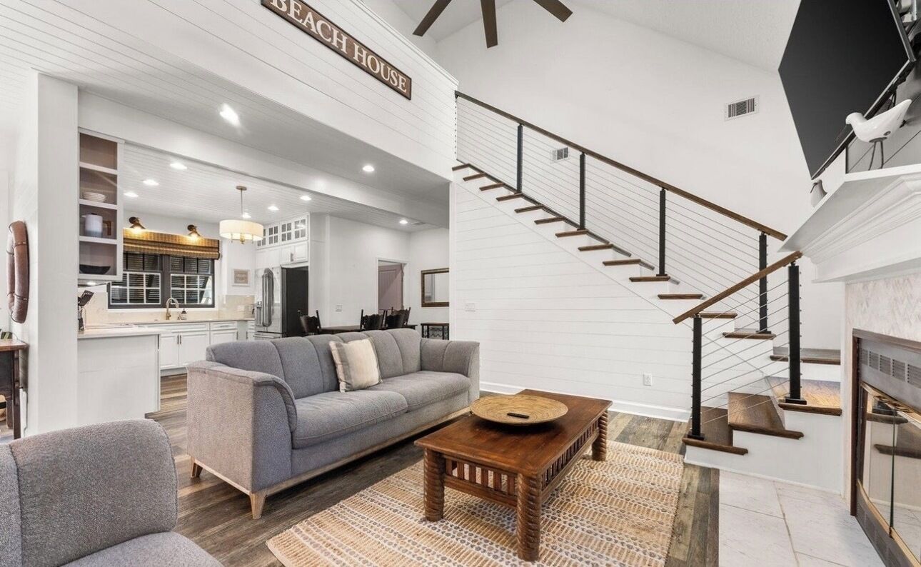 A spacious living area with a gray sofa, wooden coffee table, and a staircase with a black railing.