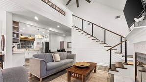 A spacious living area with a gray sofa, wooden coffee table, and a staircase with a black railing. - Steps from the sand! 4BR/3BA private home w/ heated pool, 6 seater gas golf cart (Panama City Beach, FL)