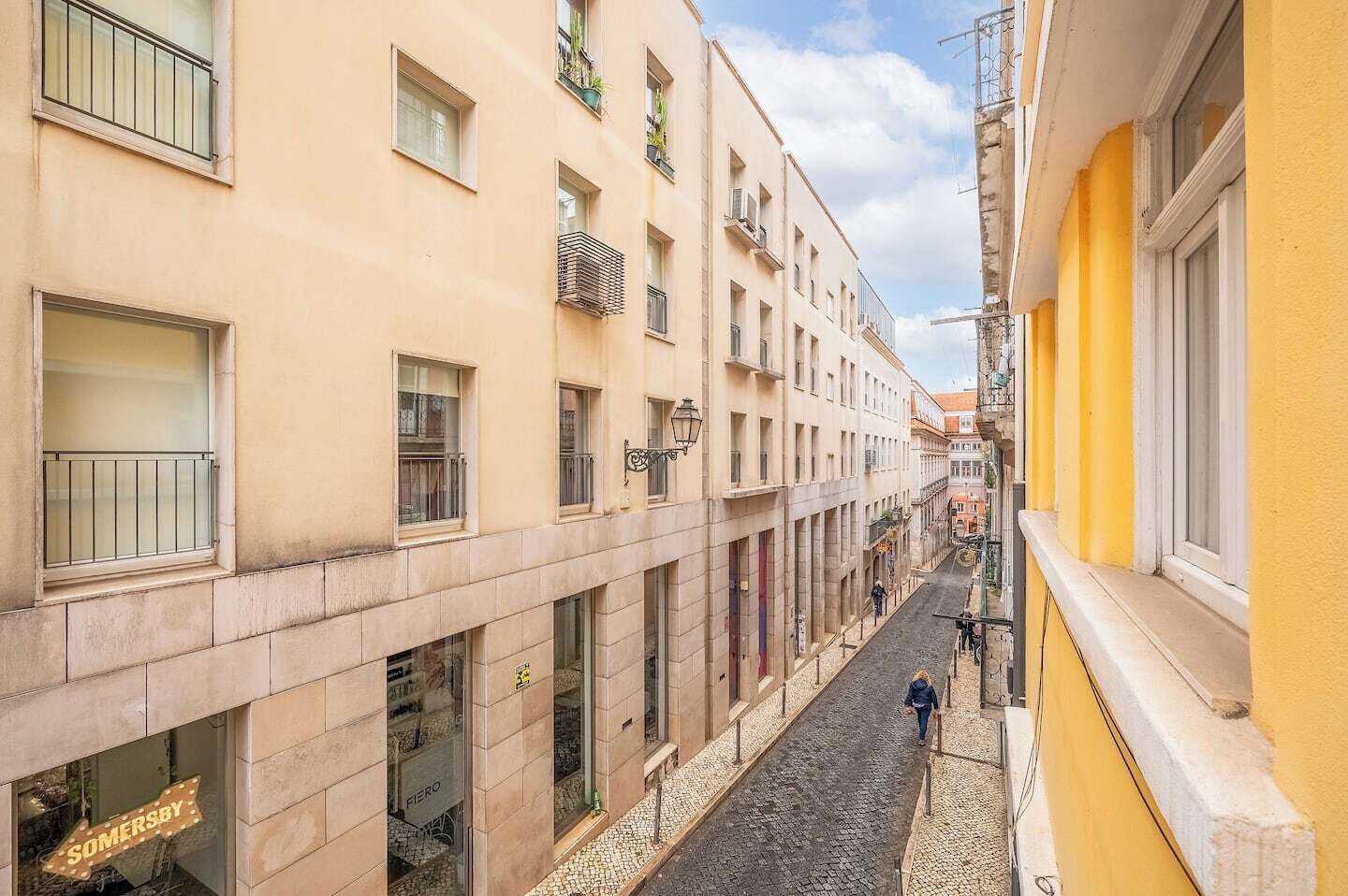 A narrow street with buildings on either side, featuring storefronts and a pedestrian walkway.